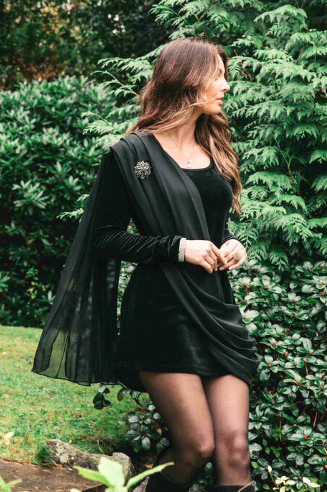 Woman in a black dress and cardigan standing in a garden