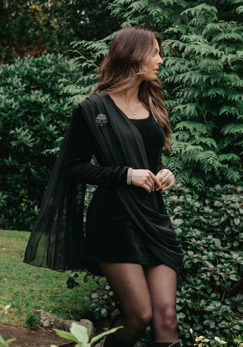 Woman in a black outfit standing outdoors with greenery in the background