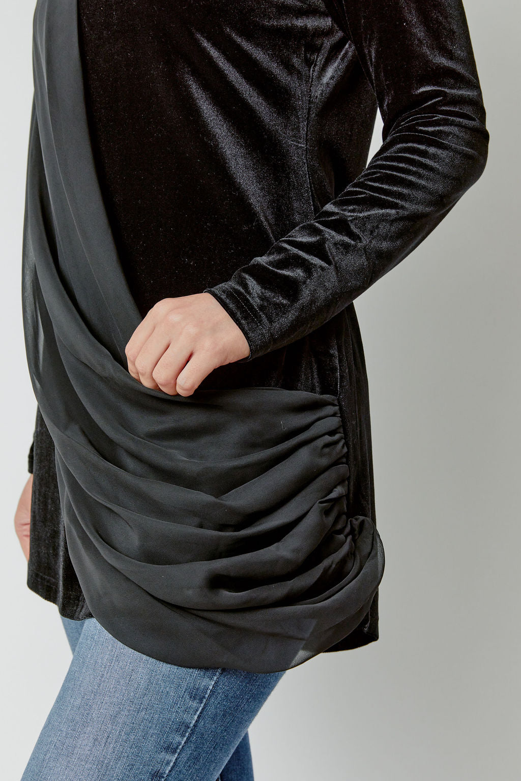 Black long-sleeve top with draped design worn over jeans on a plain background
