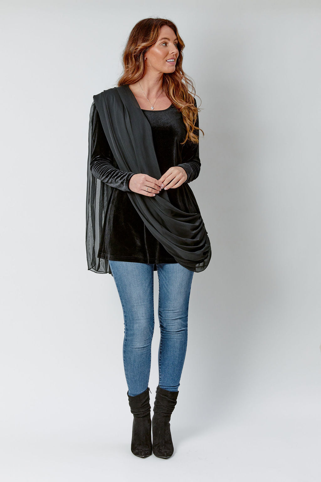 Woman wearing a black cardigan, black top, blue jeans, and black boots on a white background