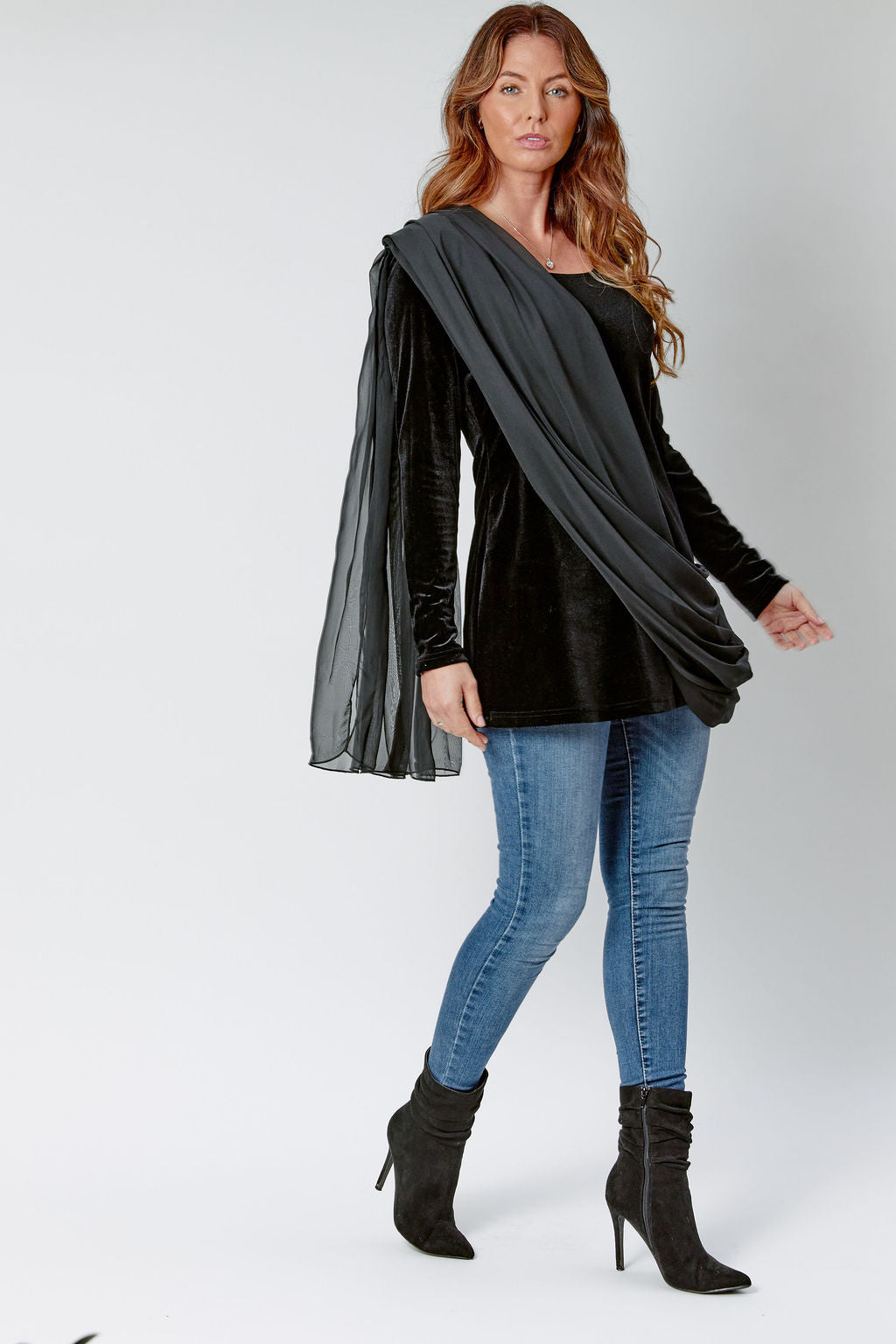 Woman wearing a black long-sleeve top, blue jeans, and black boots on a white background