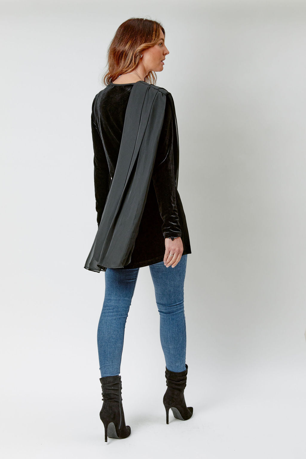 Woman wearing a black leather jacket, blue jeans, and black boots on a white background